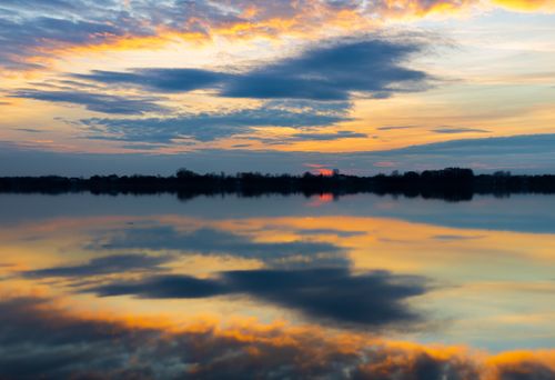 Free Peaceful sunset with dramatic clouds reflecting perfectly on a calm lake surface. Stock Photo