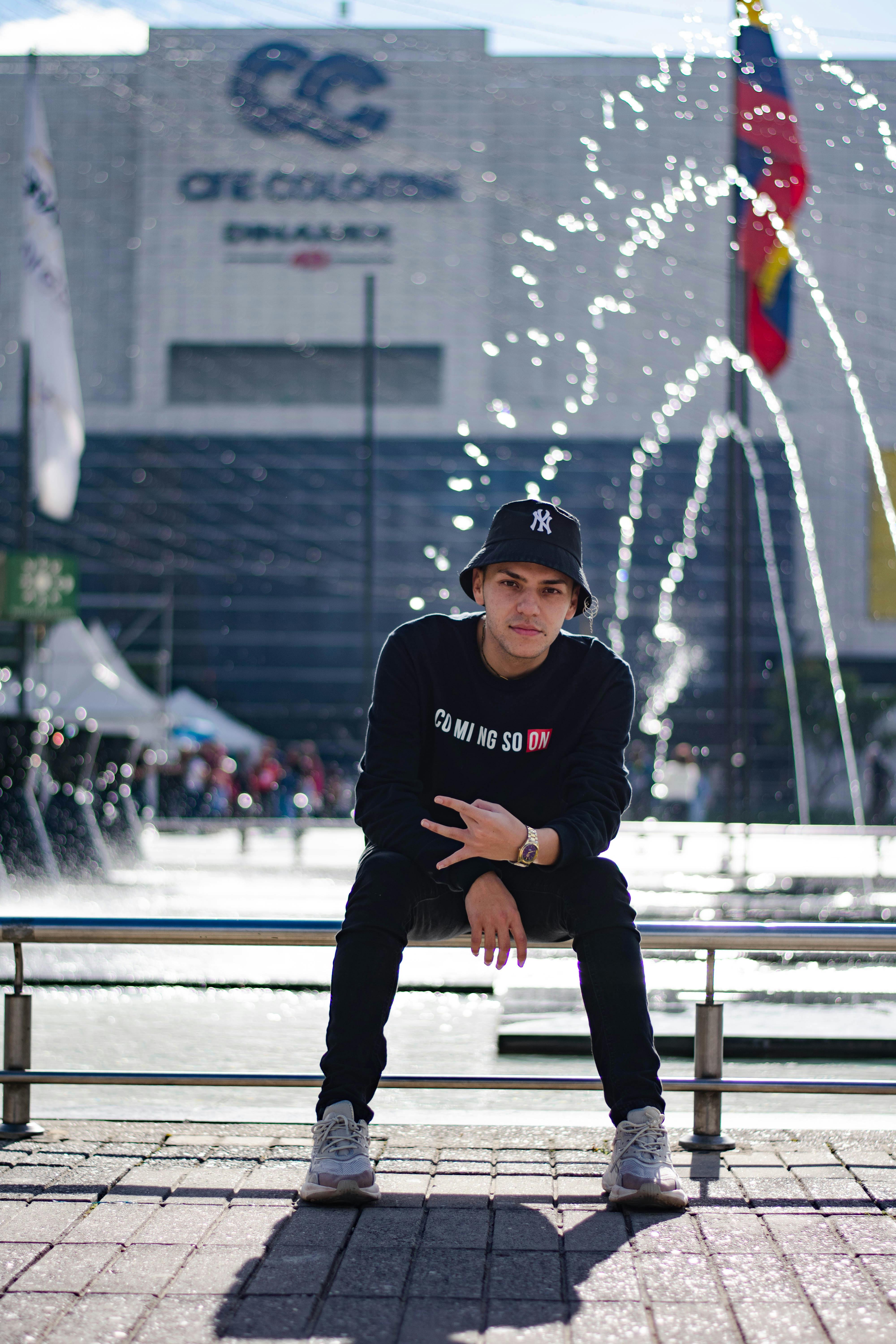 Casual young man in bucket hat sitting by water fountain under daylight.