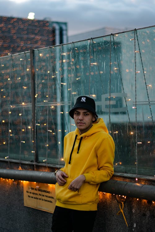 Man in Yellow Hoodie Leaning on a Fence