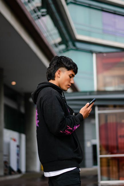 Young man in black hoodie using smartphone outside shopping mall.