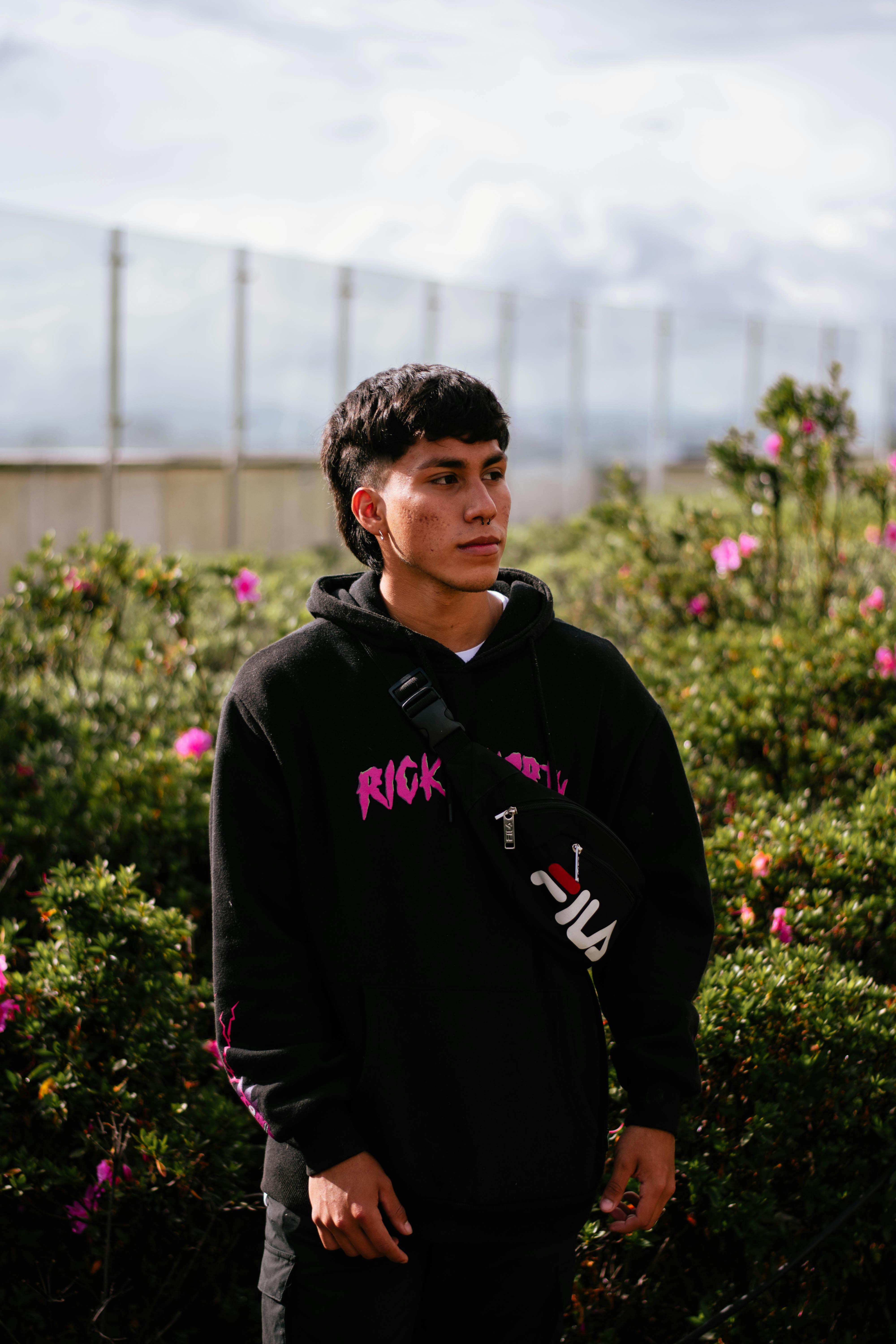 Portrait of a young man in a black hoodie standing in a blooming garden.