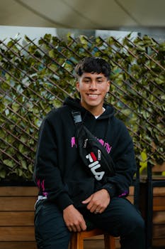 Portrait of a smiling man in a hoodie sitting outdoors with a stylish bag.