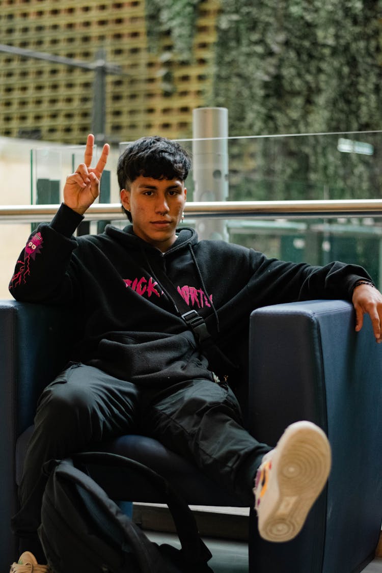 Man In Black Hoodie And Black Pants Sitting On A Blue Leather Chair 