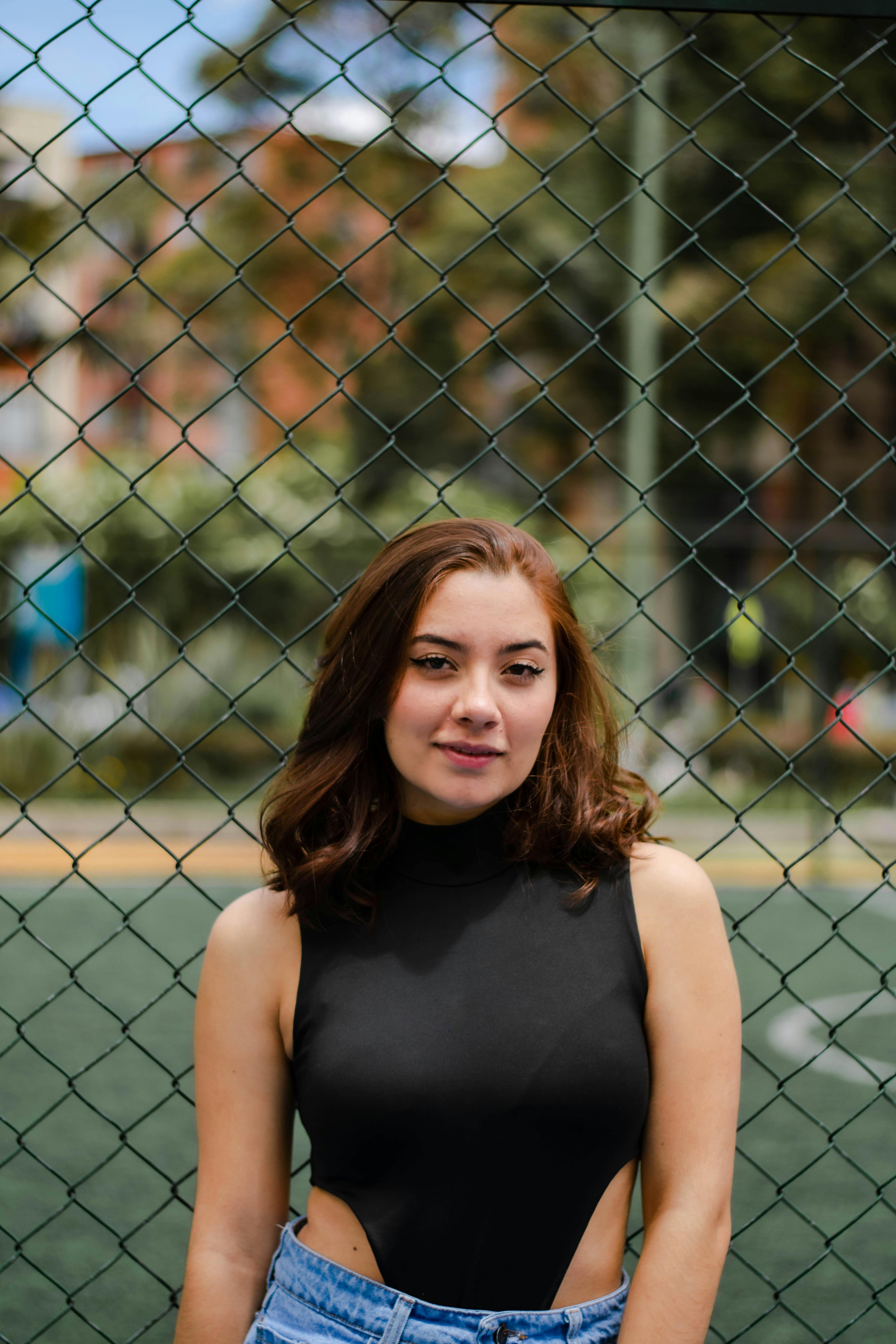Woman in a Black Top in Front of a Chain Link Fence · Free Stock Photo