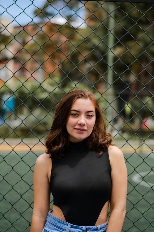 Woman in a Black Top in Front of a Chain Link Fence