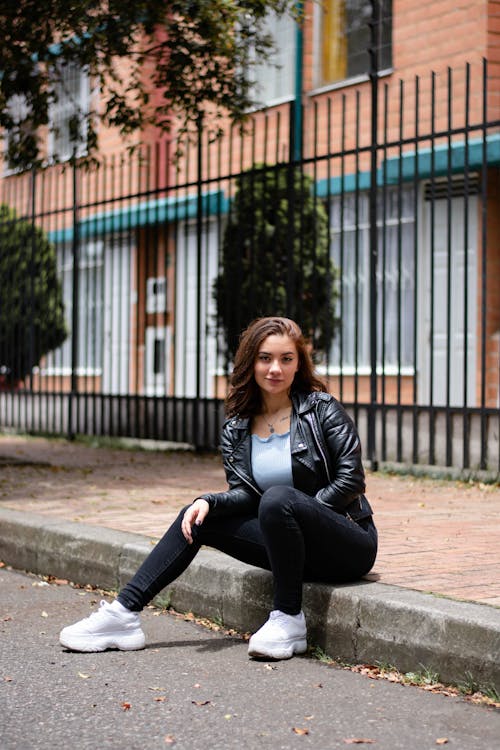 A Woman in Black Leather Jacket Sitting on a Sidewalk
