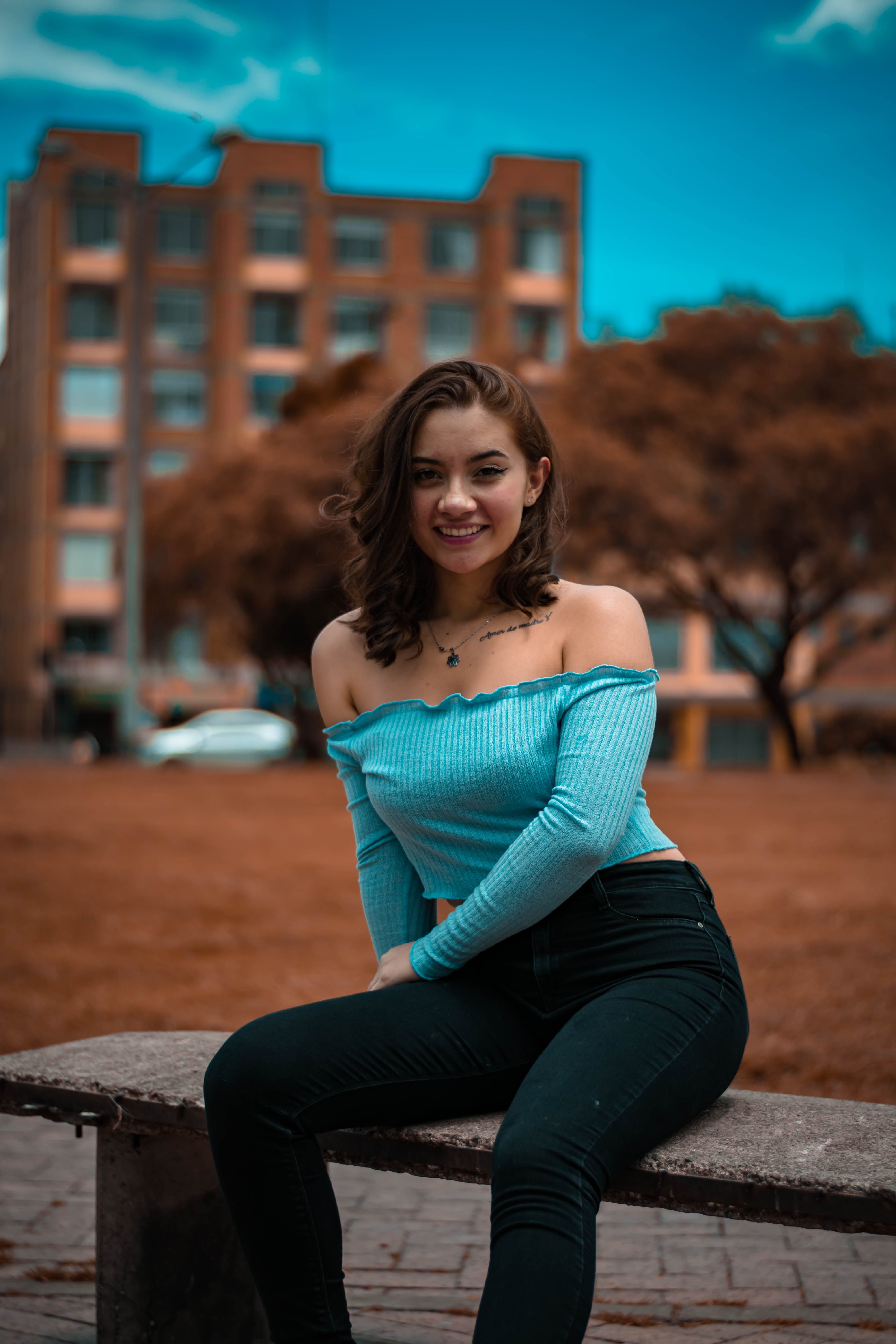 Stylish woman in casual outfit sitting on a bench in an urban setting, smiling confidently.