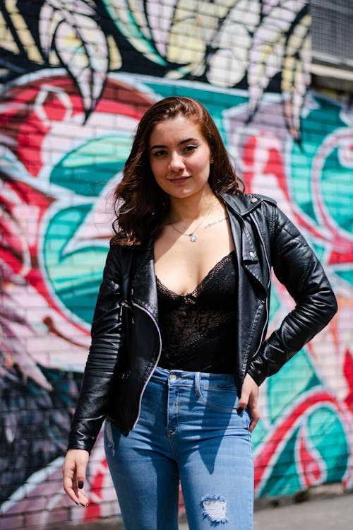 Woman in leather jacket and jeans against graffiti wall, edgy outfit