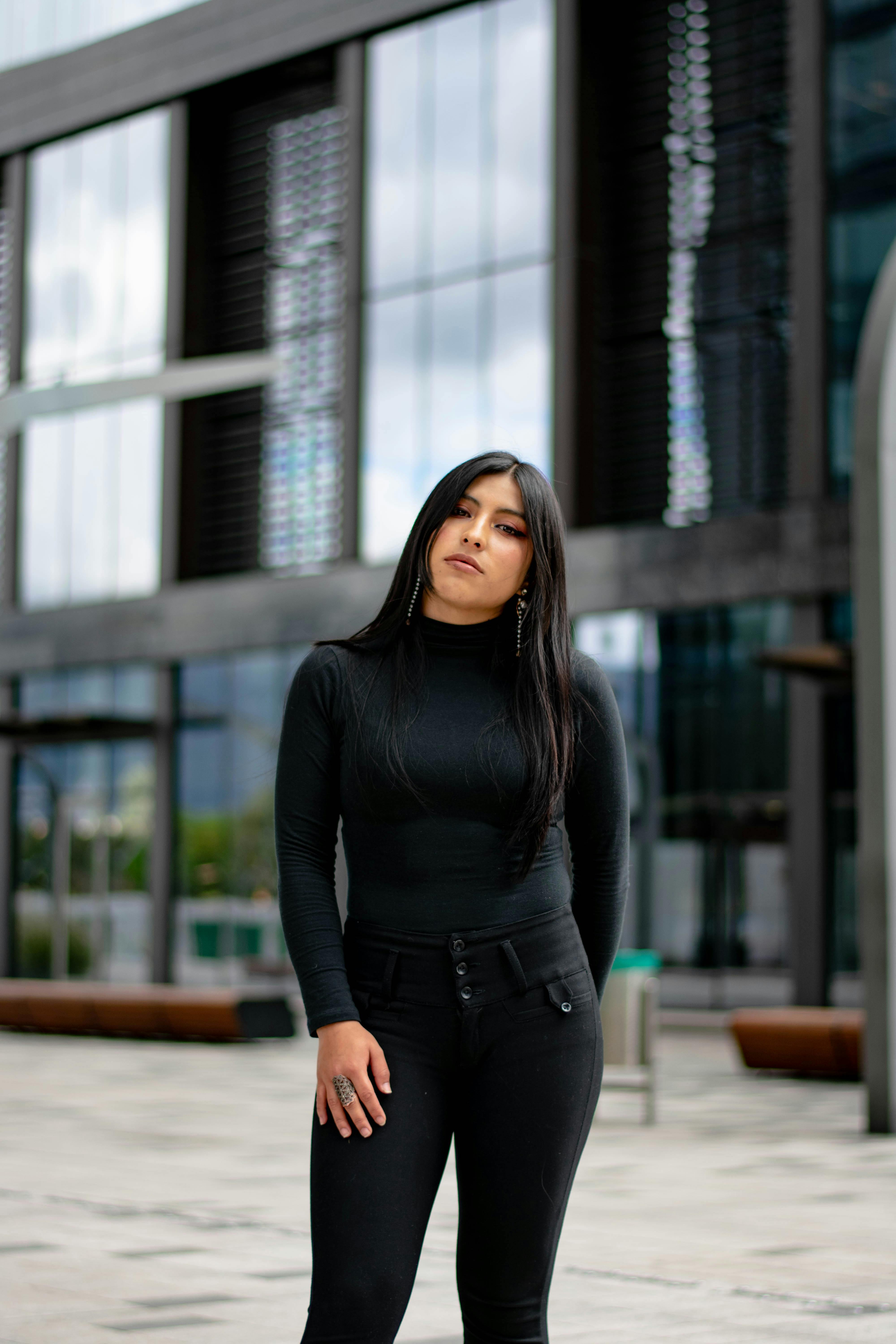 Confident woman in black attire posing outside an urban building.