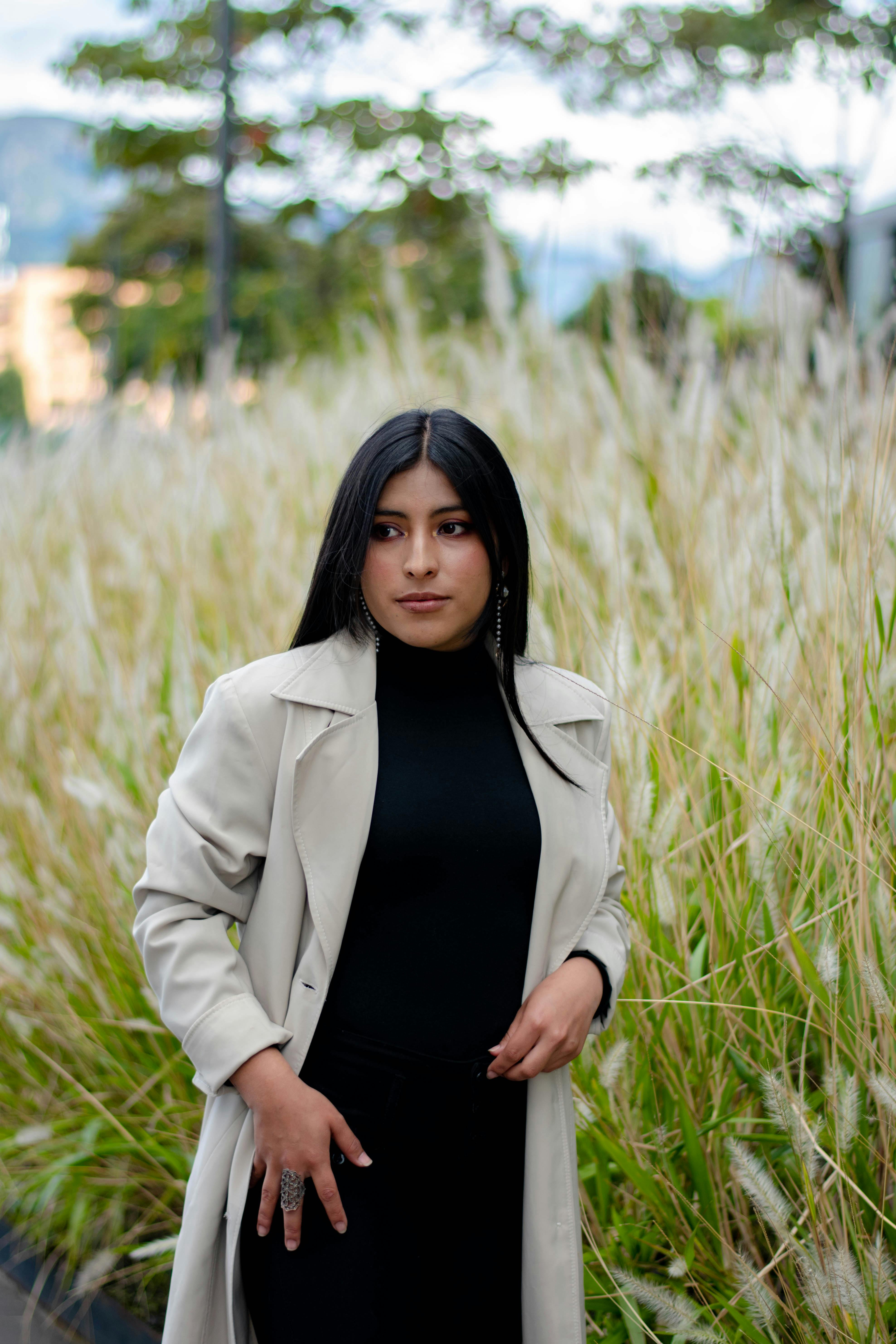 Fashionable woman in a trench coat posing in a grassy field.