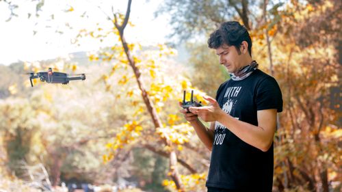 Free A young man controls a drone in a vibrant autumn park, capturing scenic views. Stock Photo
