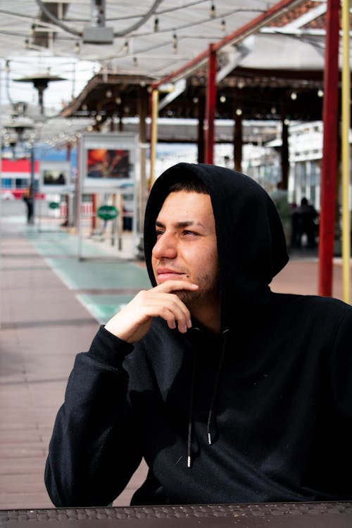 Man in Black Hoodie Sitting With Hand on Chin 