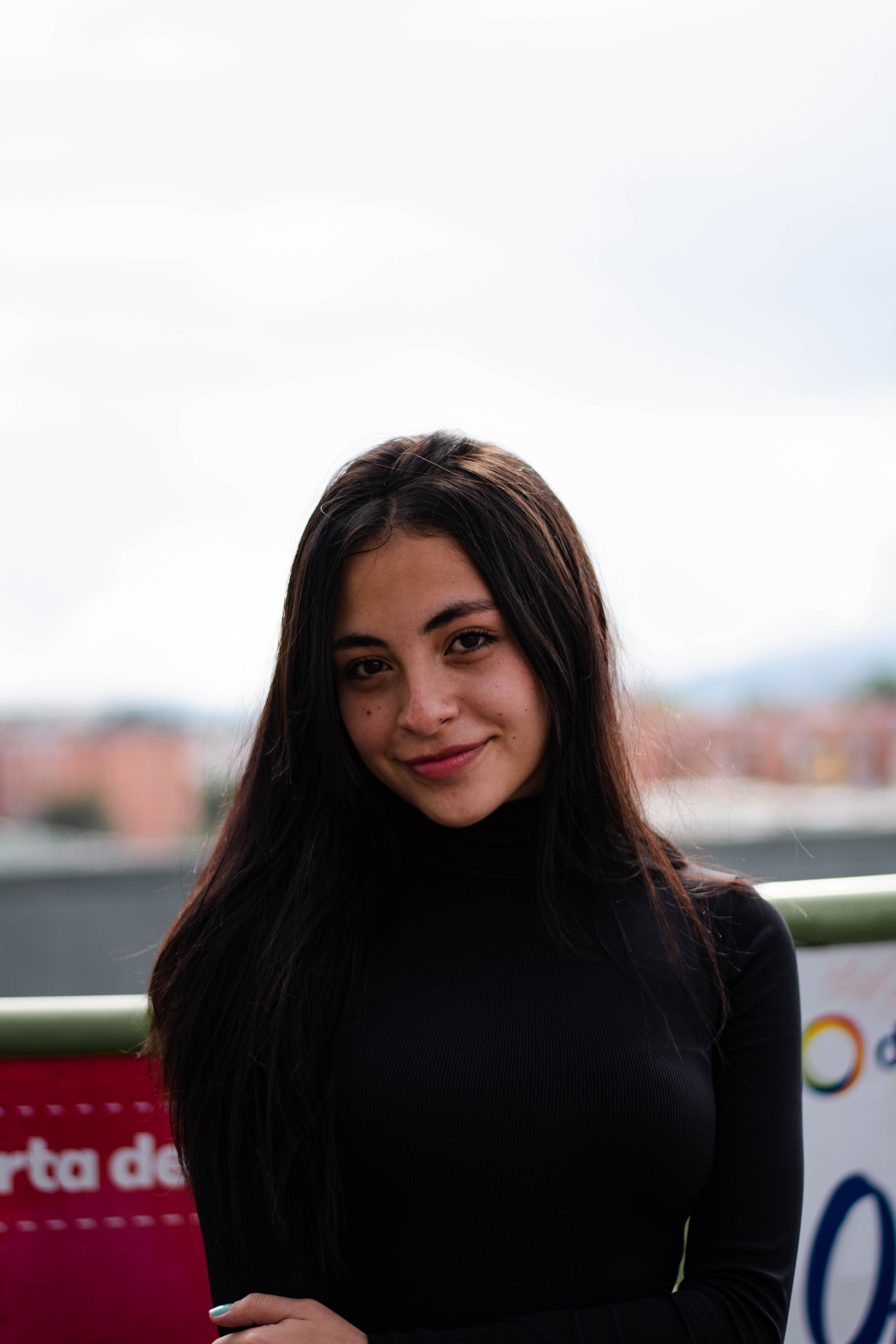 Portrait of a young woman smiling in a black turtleneck against an outdoor backdrop.