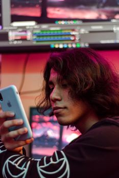 Teenager using a smartphone in a tech-heavy setting with multiple screens.
