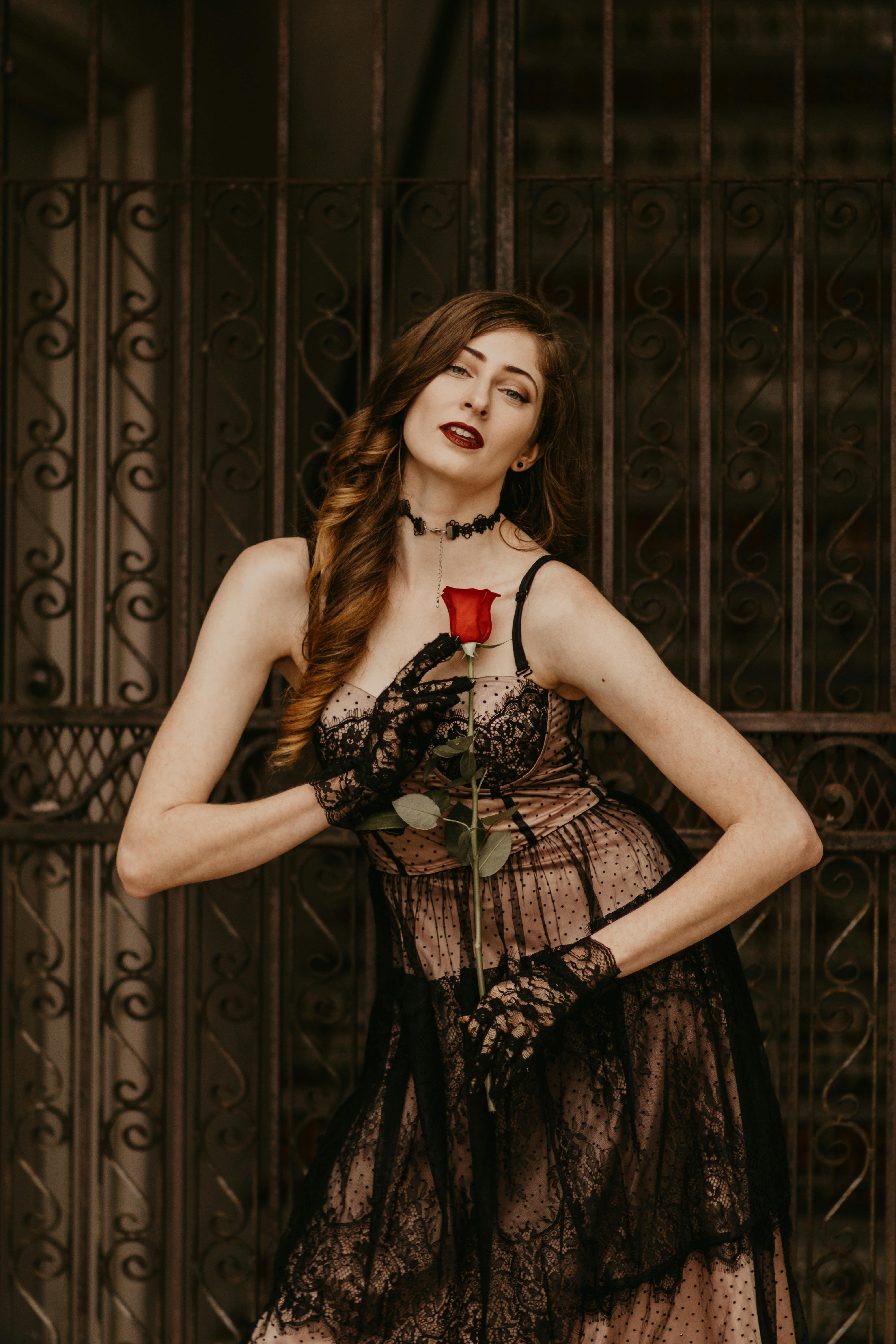woman with long curly hair posing with red rose in hands