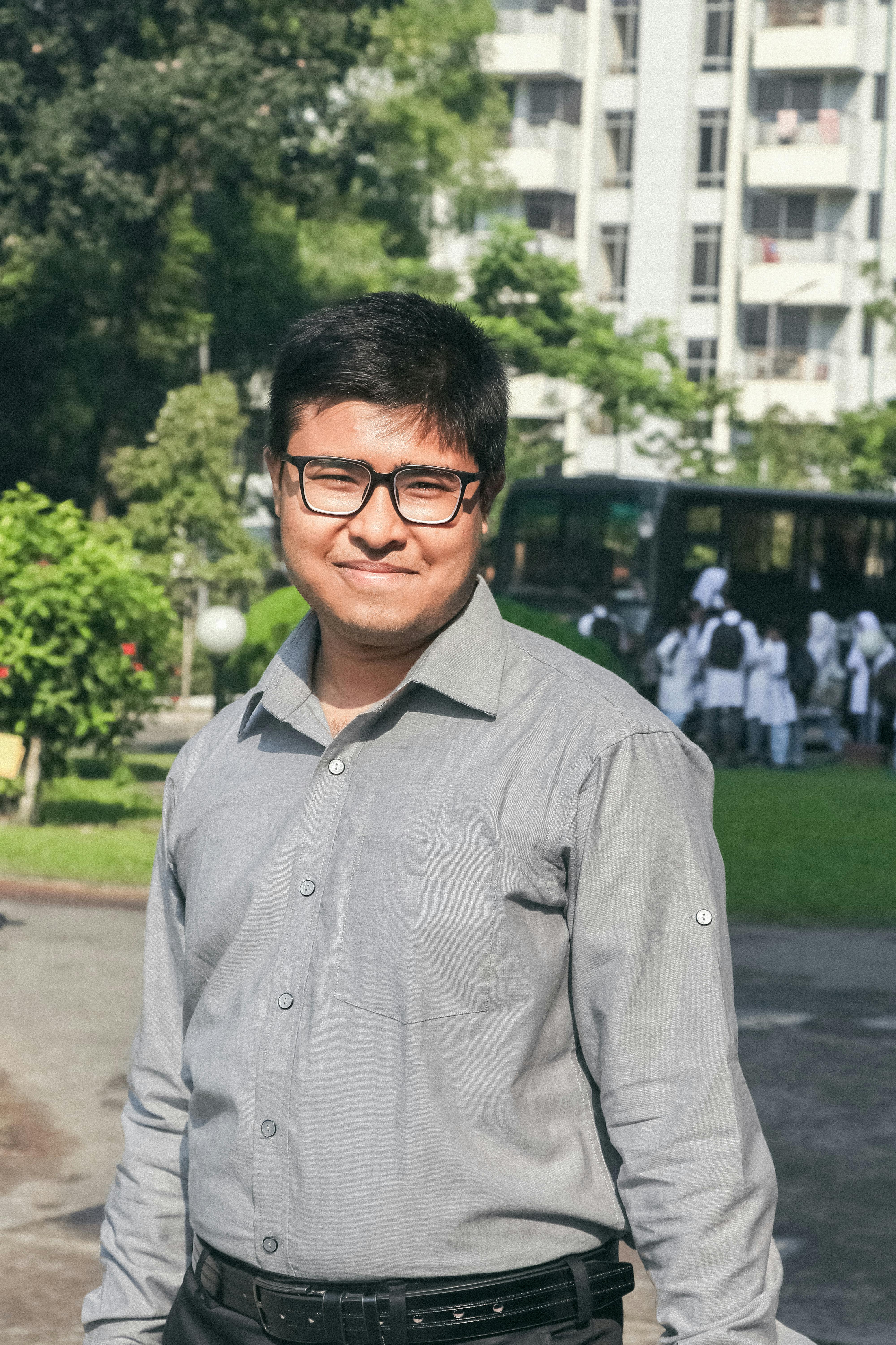 Smiling man wearing eyeglasses and long sleeve shirt outdoors in a urban park setting in Bangladesh.