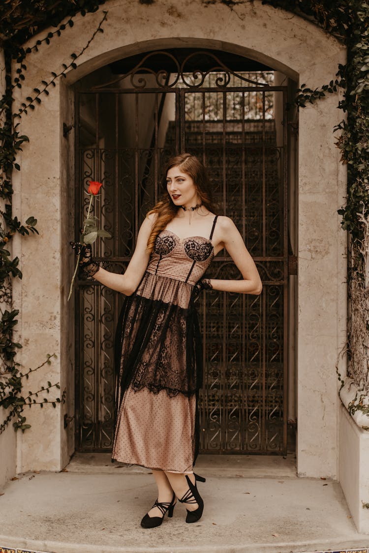 Woman With Red Rose In Hand Posing In Front Of House Ornamental Gate