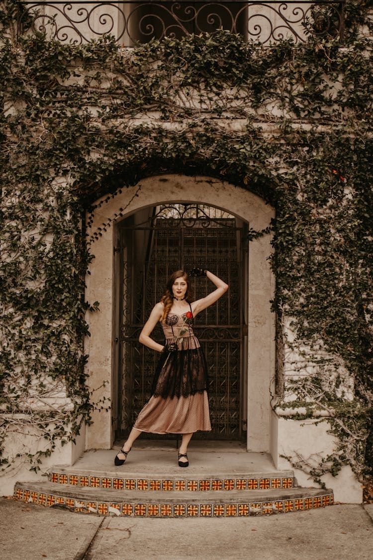 Adult Woman Wearing Vintage Lace Dress Standing In Pose Before House Gate