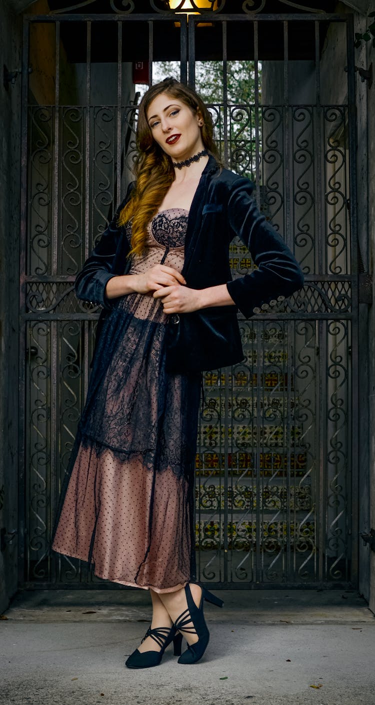 Woman In Dress And Black Blazer Standing Near Metal Gate 