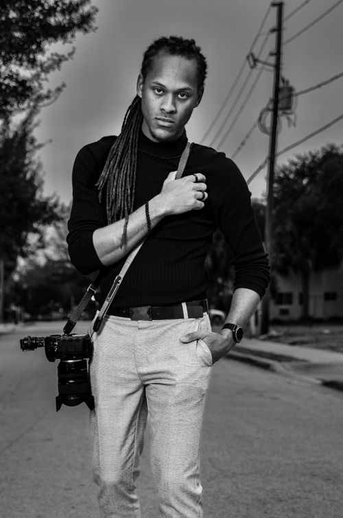 Free Black and white portrait of a male photographer in a city setting, holding a DSLR camera. Stock Photo