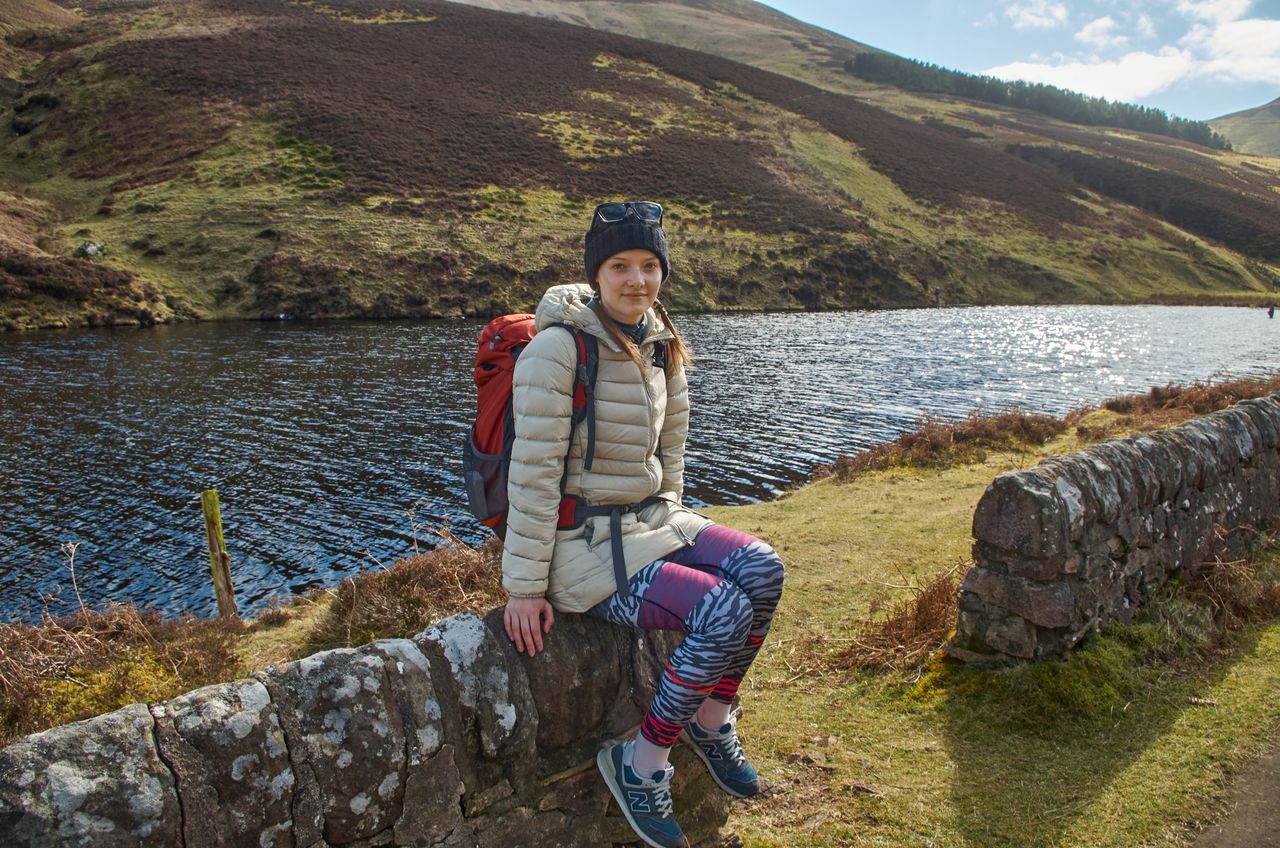 Woman in a puffer jacket and beanie sitting by a lake