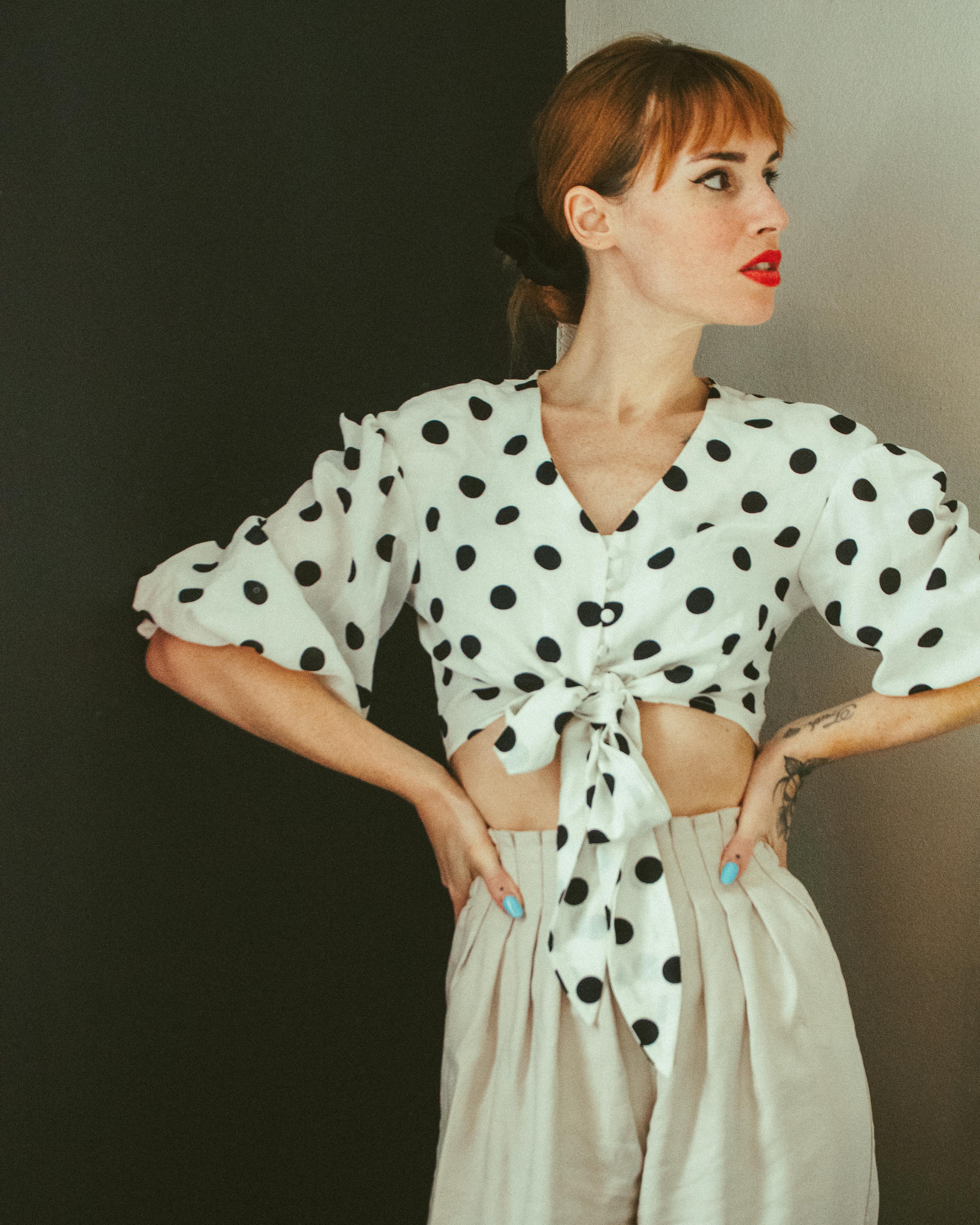 Free Stylish adult woman wearing a polka dot crop top gazes to the side with hands on waist. Stock Photo