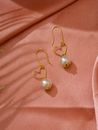 Pair of Heart Shaped Gold and Pearl Earrings on Pink Background