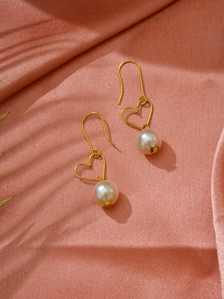 Pair Of Heart Shaped Gold And Pearl Earrings On Pink Background