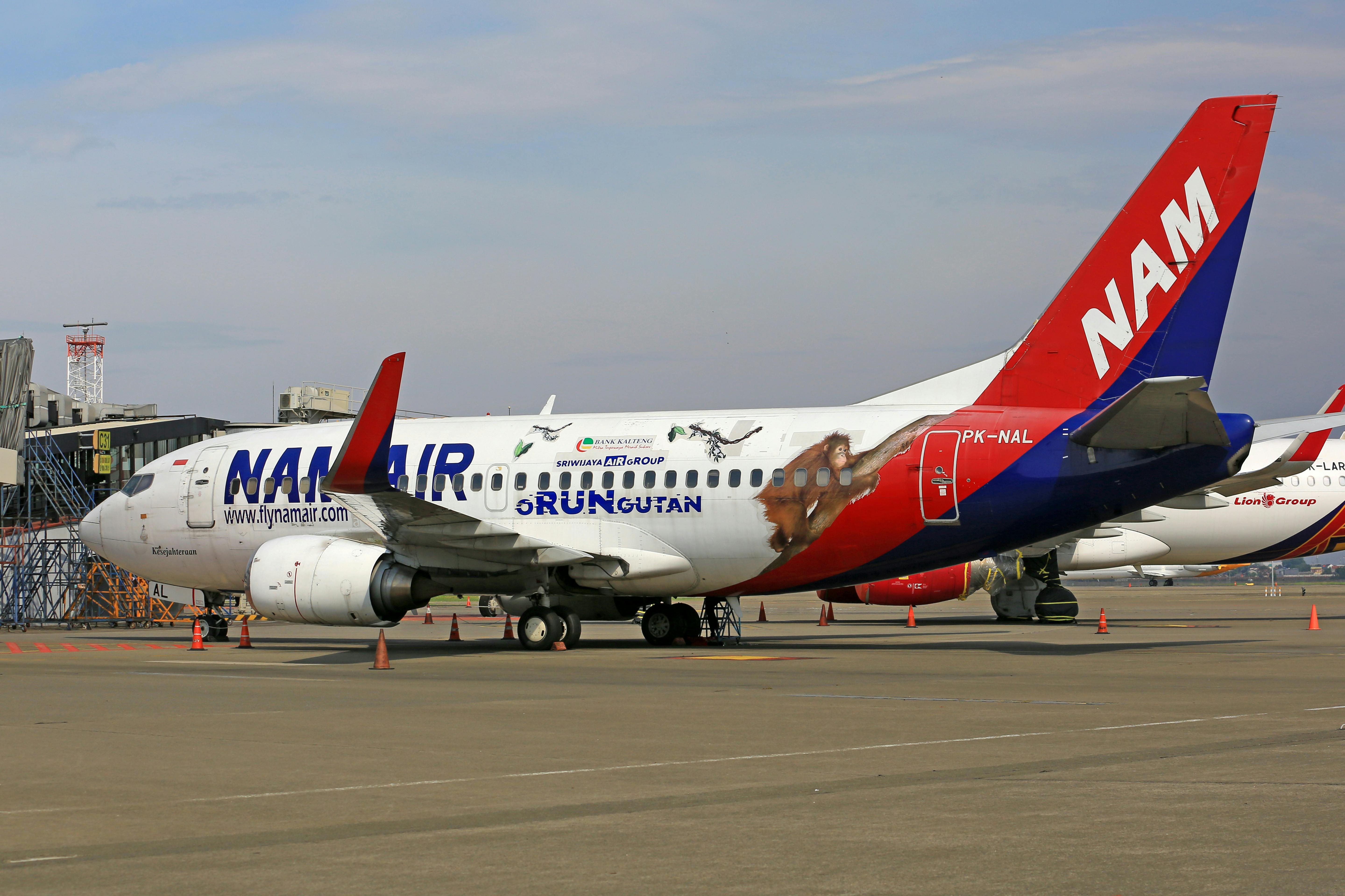 NAM Air Boeing 737 plane parked on the airport tarmac in daylight, showcasing vibrant logo and design.