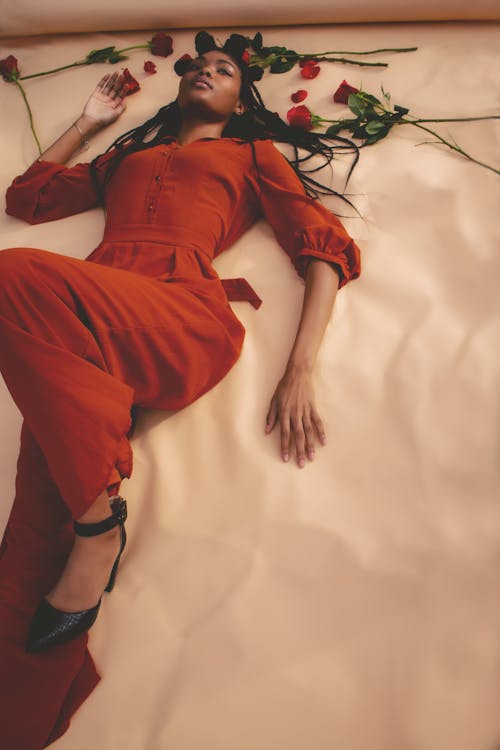 Woman in Orange Outfit Lying on Bed Beside Red Roses while Looking Afar