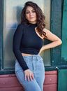 Woman in Asymmetrical Top Leaning Against Wall