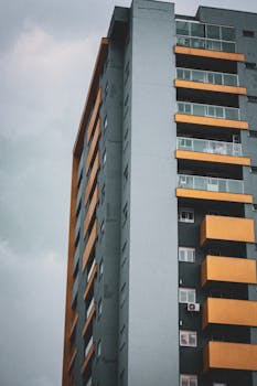 Low angle view of a modern tall building with orange accents against a cloudy sky.