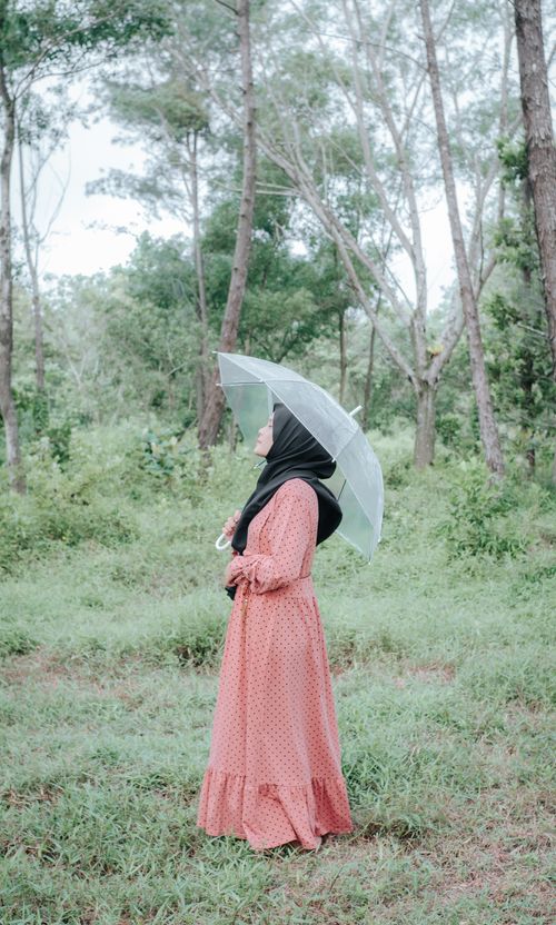 Free A woman in a red dress and hijab holds an umbrella in an Indonesian forest, showcasing natural beauty. Stock Photo