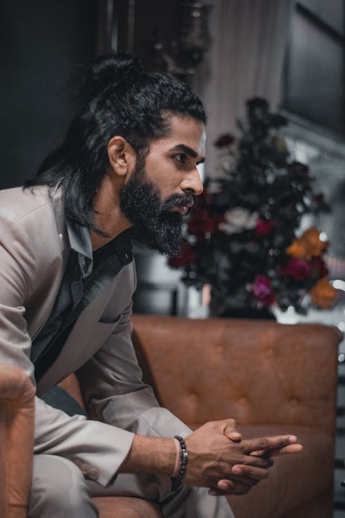 Free Bearded Man in Gray Suit Jacket Sitting on Brown Couch while Looking Afar Stock Photo