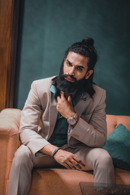 Free Elegantly dressed bearded man in a gray suit sitting on a couch, exuding a serious and contemplative aura. Stock Photo
