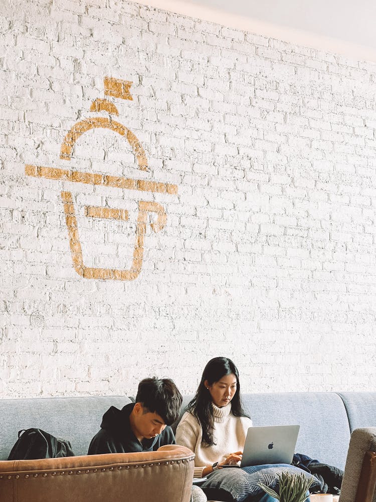 Two Young People Sitting At Coffee Point And Working On Laptops