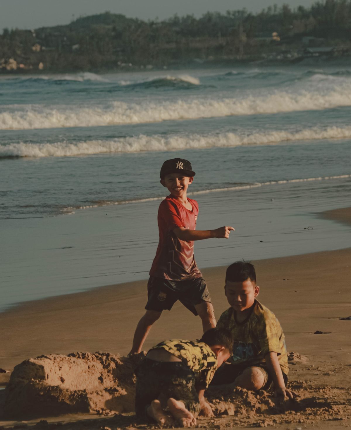 Three kids enjoying a sunny day by the seashore, playing in the sand.