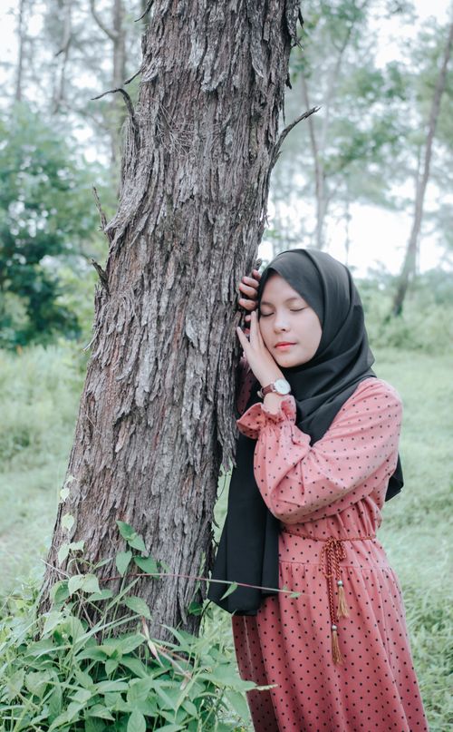 Free A woman in a hijab with closed eyes, embracing a tree in a peaceful outdoor setting. Stock Photo