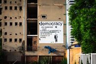 An abandoned building features a prominent democracy poster amidst urban decay.