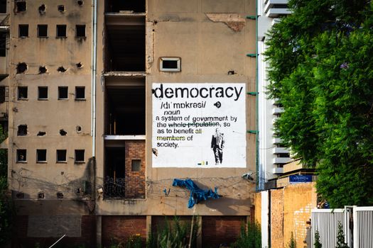 An abandoned building features a prominent democracy poster amidst urban decay.