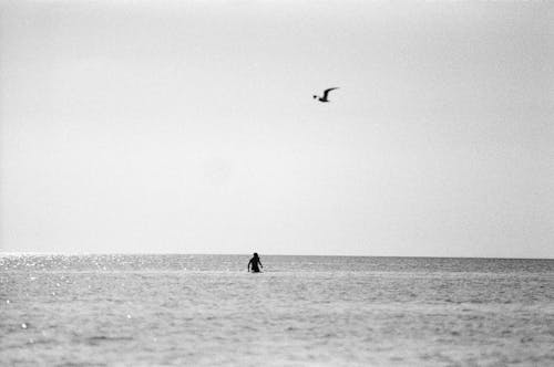 Grayscale Photo of a Person Soaking on the Beach Water 