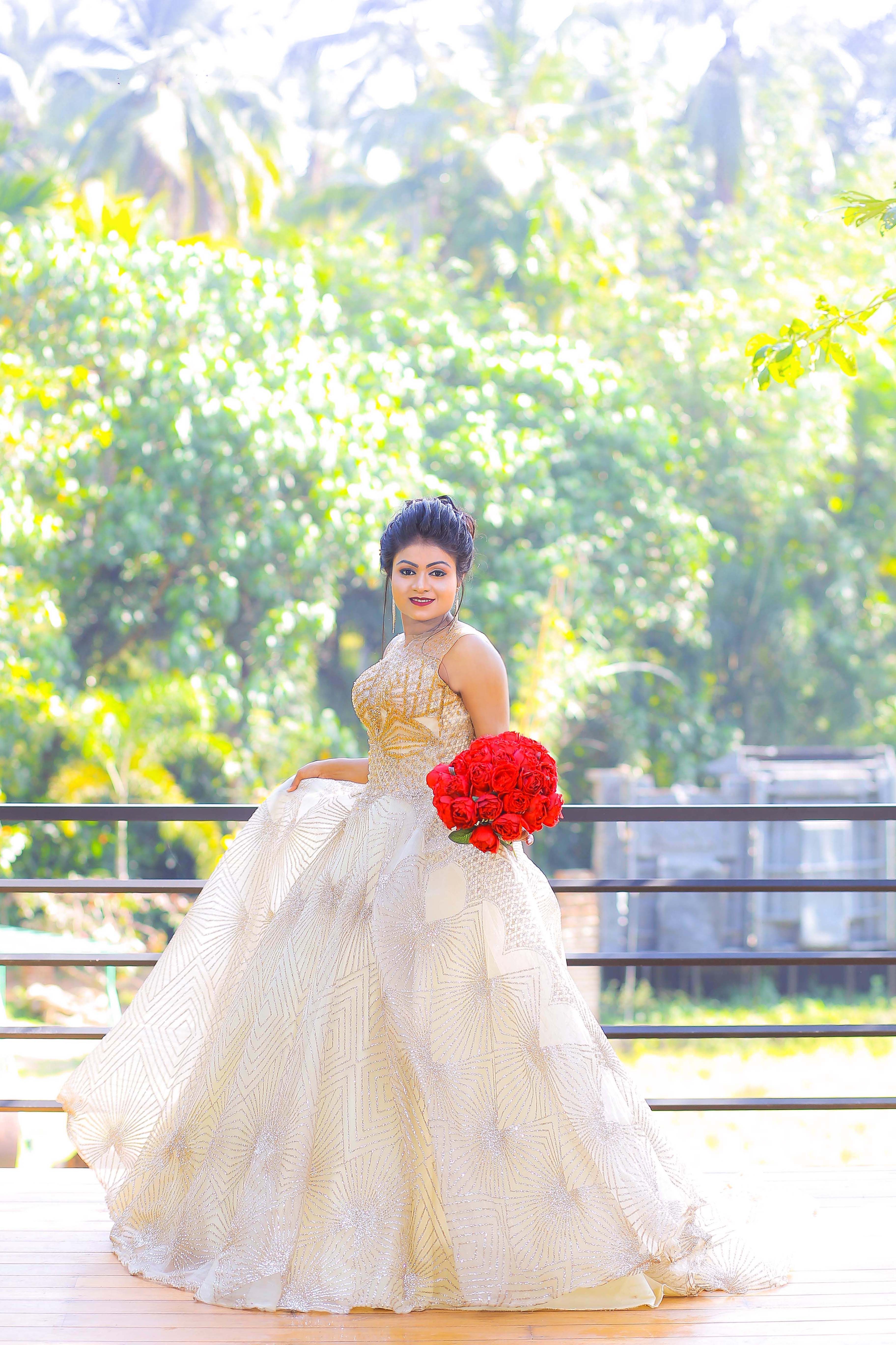 Beautiful bride holding red bouquet in lush garden, wearing elegant dress.