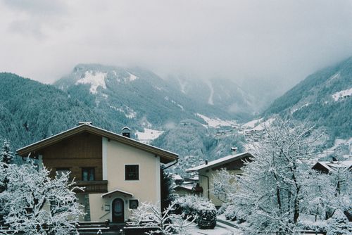 Free A peaceful winter scene featuring snow-covered houses nestled in a mountain town, surrounded by snowy peaks. Stock Photo