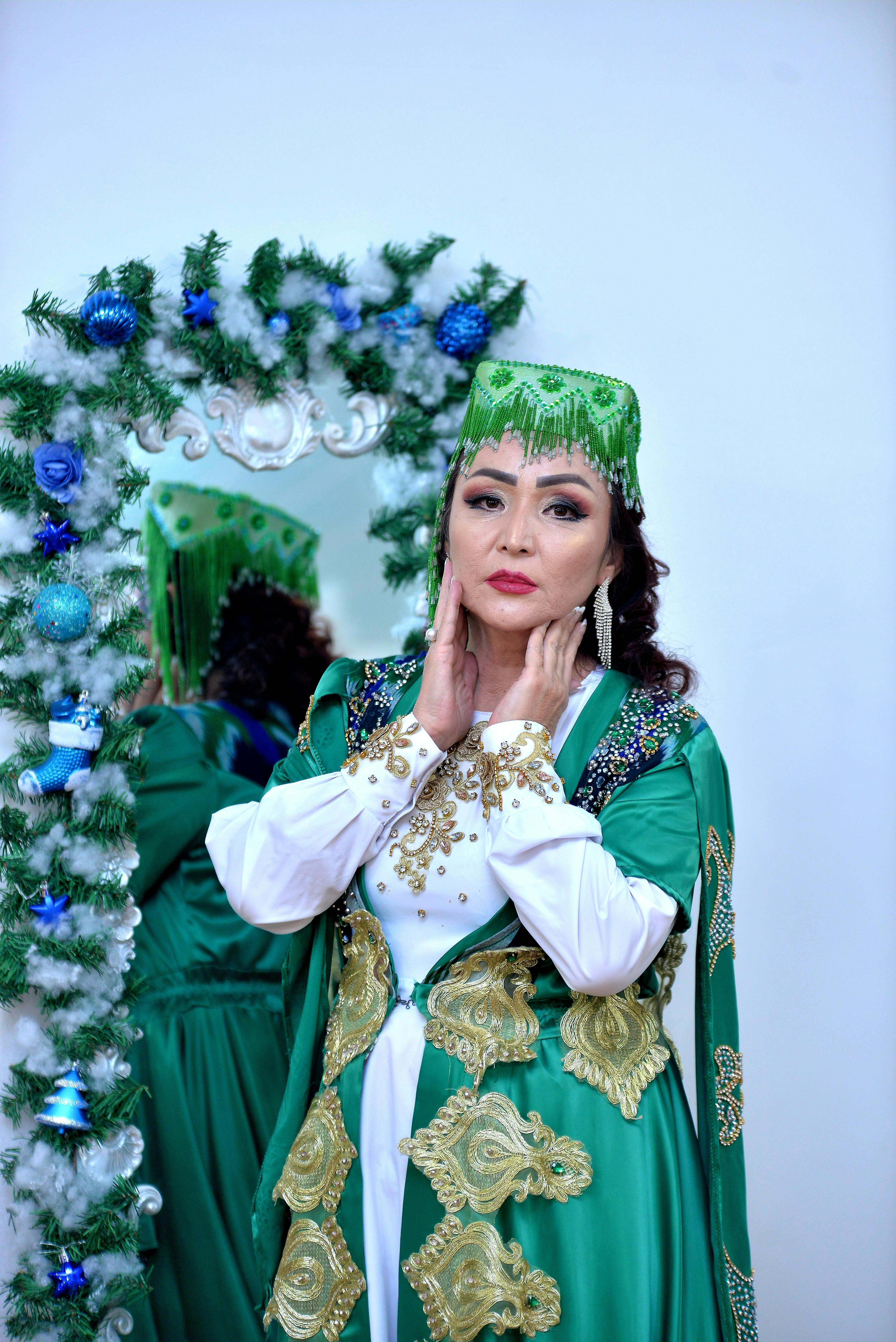 Elegant woman posing in green traditional attire with decorative holiday accents and mirror reflection.