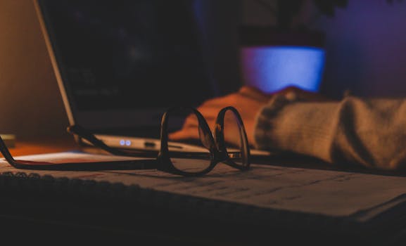 Close-up of eyeglasses and a laptop at night, illustrating a cozy work environment.