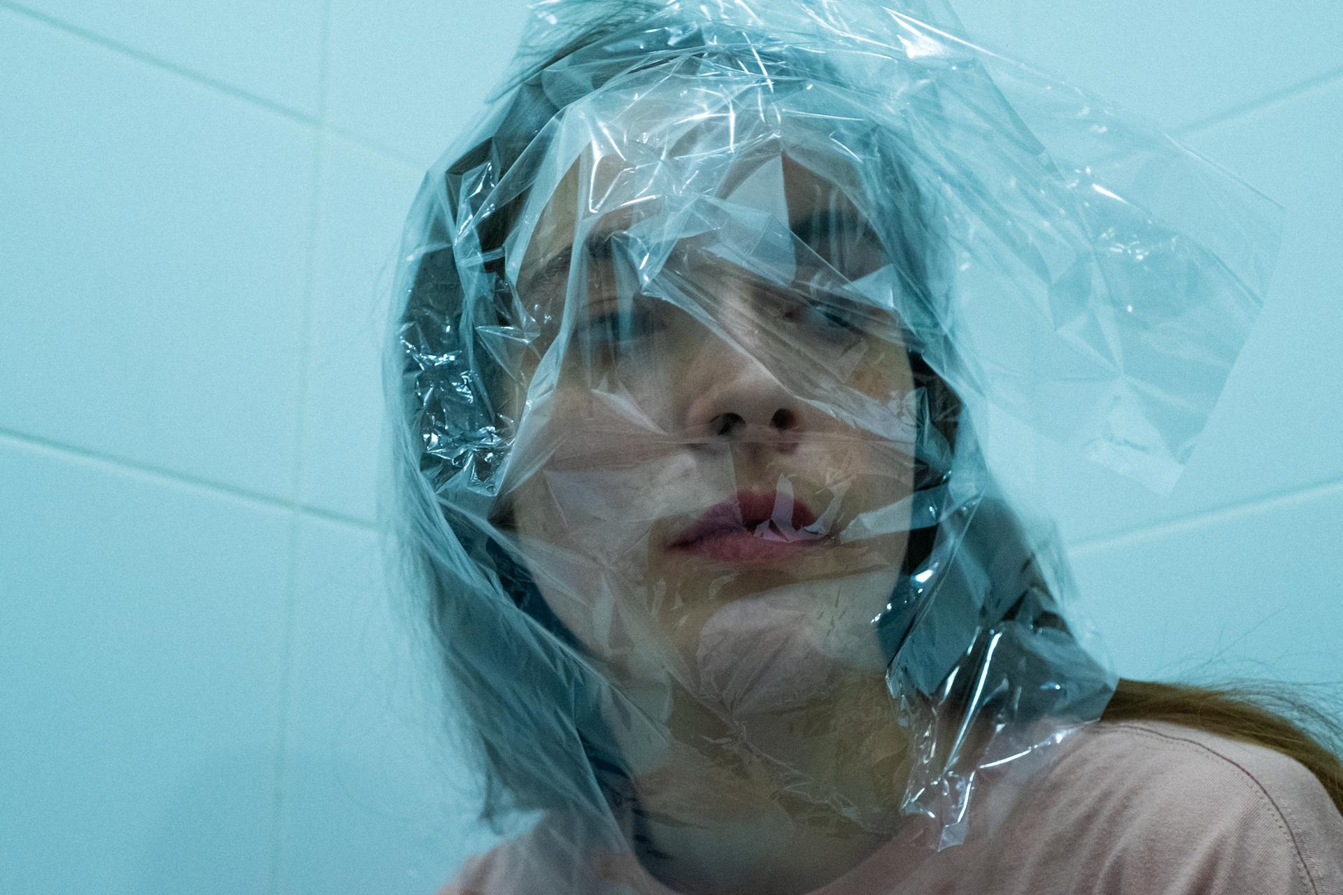 Introspective portrait of woman with plastic wrap in a tiled setting, expressing emotions.