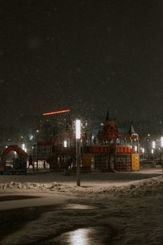 Snow-covered playground illuminated by streetlights during a winter night.