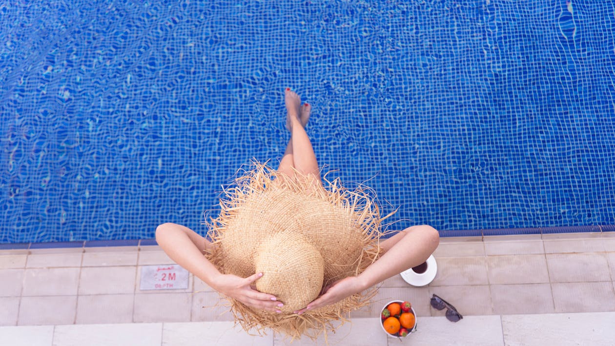 A Person Wearing Straw Hat while Sitting on the Edge of the Pool 