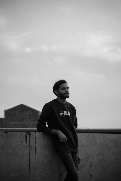 Man in Sweatshirt Leaning on a Concrete Fence