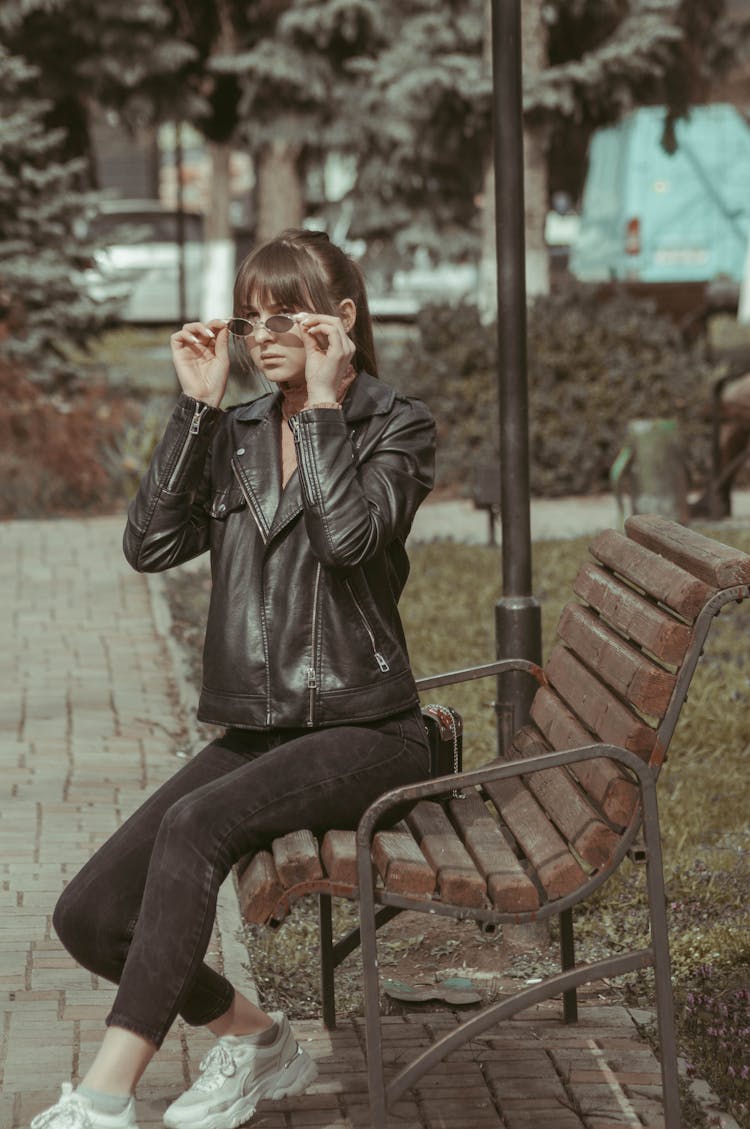 Woman In Black Leather Jacket And Pants Sitting On Wooden Bench